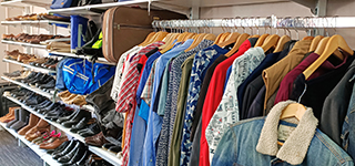 Clothes on a rack and in the background rows of secondhand shoes
