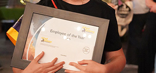 Close up of employee holding a framed certificates that says "employee of the year"