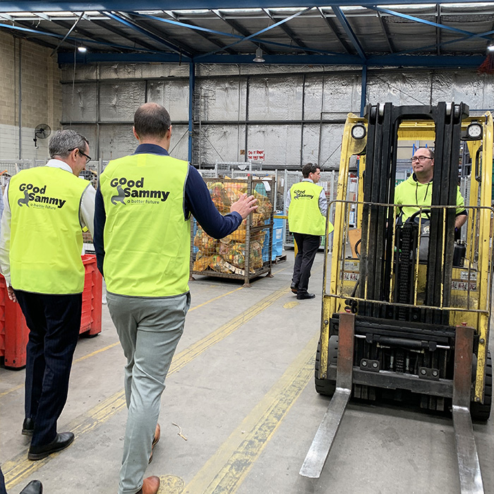 The Premier and CEO Kane Blackman walking through the Good Sammy warehouse. An employee with disability is seen driving a forklift to the right of them.