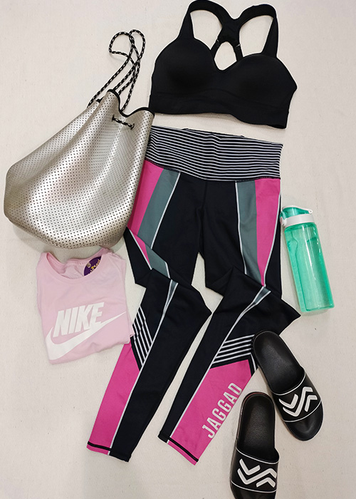 Flatlay of pink and black activewear look, featuring Nike pink top and black slides and a bright teal water bottle