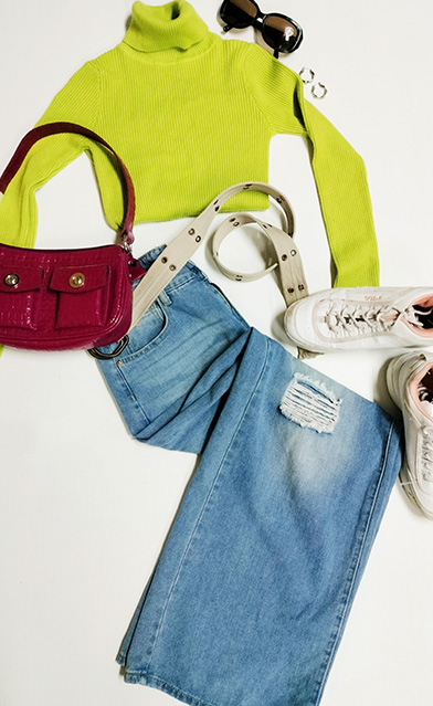 Flat lay of baggy jeans and turtleneck lime green sweater with chunky glasses and accessories.