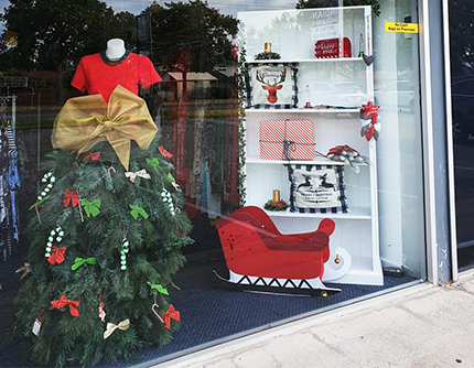 Mannequin is dress made out of a christmas tree, filled with bows and candy canes. Sleigh and christmas ornaments are next to it.