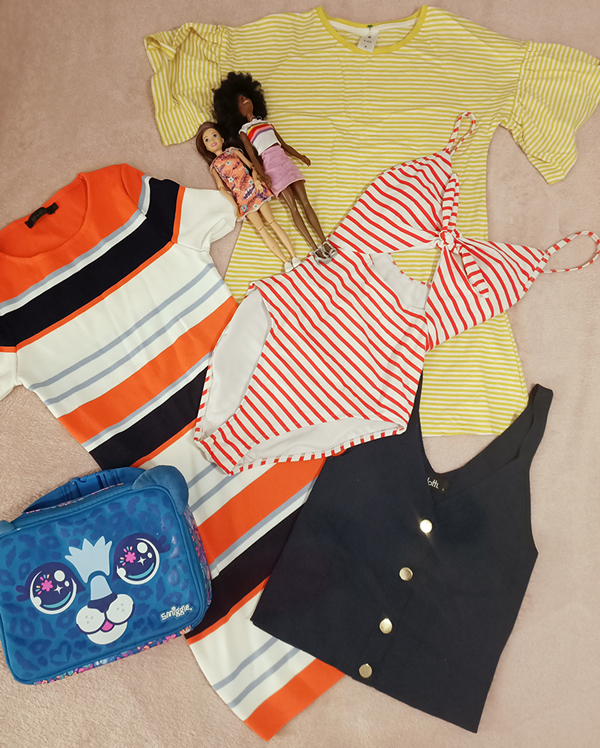 Flatlay of kids bathers, shirts, handbag and dolls