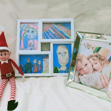 Elf on the Shelf sitting next to a collection of photo frames