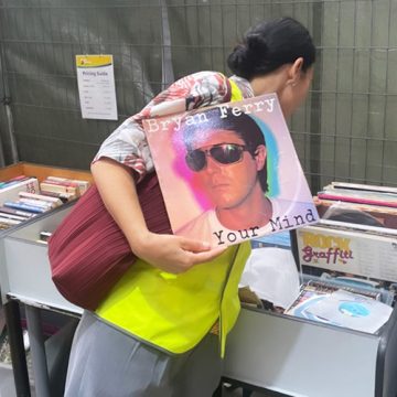 Student hunting through old records at Good Sammy Factory Outlet, holding one up by Bryan Ferry.