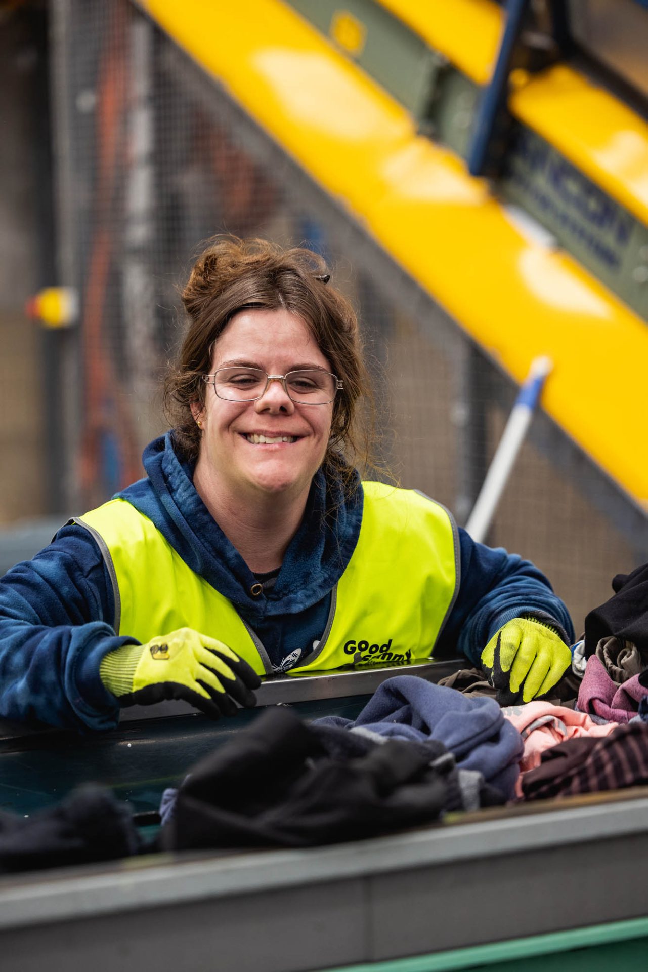 Employee smiling at camera while working on conveyor belt sorting donations